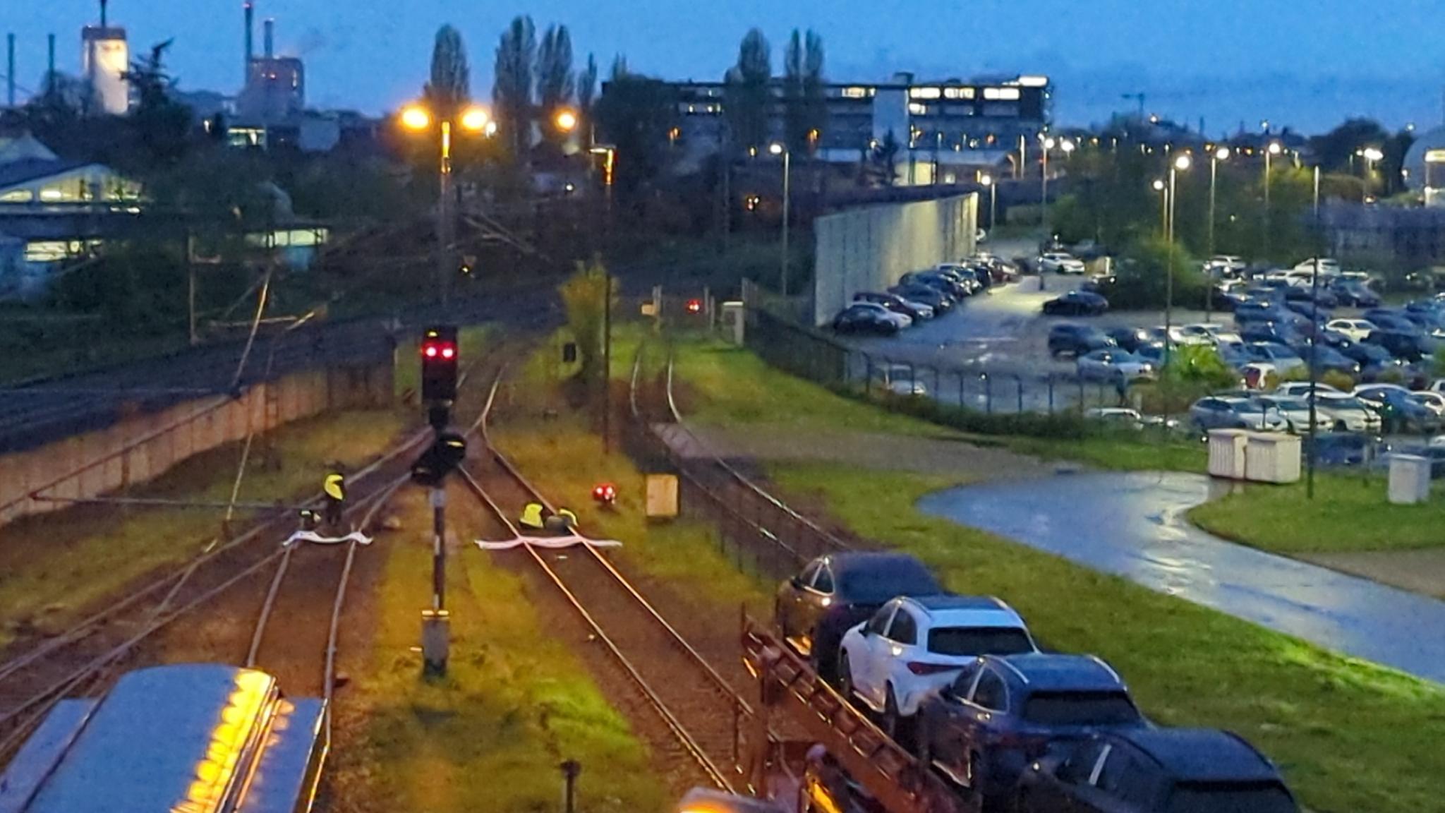 Im Hintergrund ist das Merceds-Benz-Werk in Bremen zu sehen, davo sind Gleise. Auf den Gleisen stehen (vorne im Bild) zwei Züge vor einer roten Signallampe. Dahinter, in der Mitte des Bildes sind mehrere Menschen mit Transparenten auf den Gleisen zu sehen.